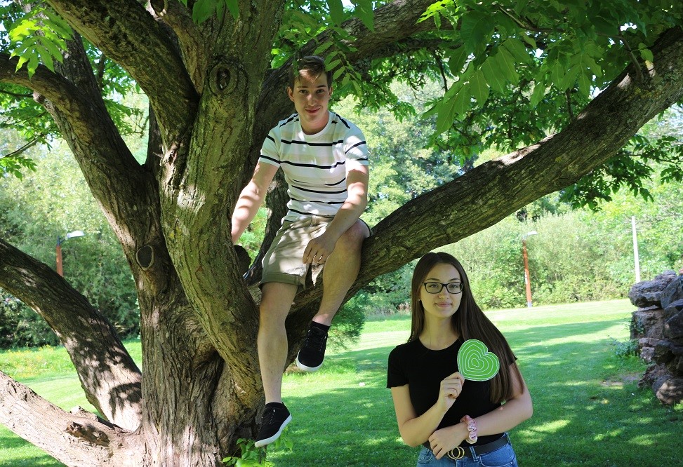 Junge sitzt auf einem Baum, Mädchen steht daneben